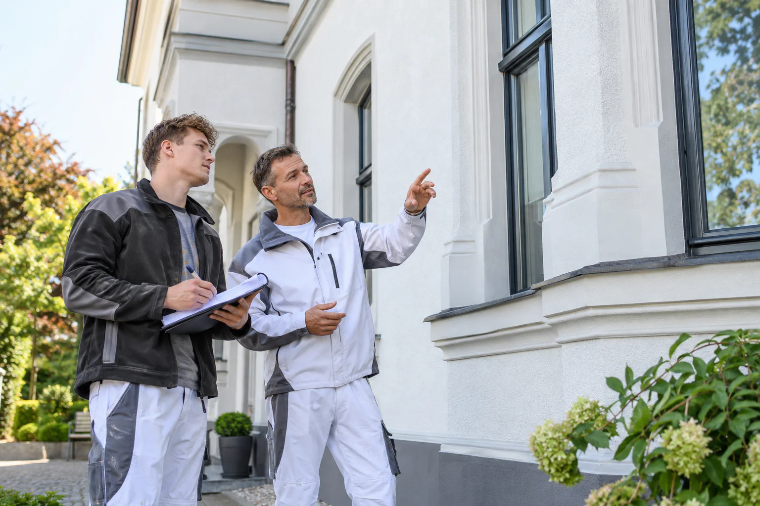 Nachwuchskraft betrachtet mit einem erfahrenen Kollegen ein Wohnhaus